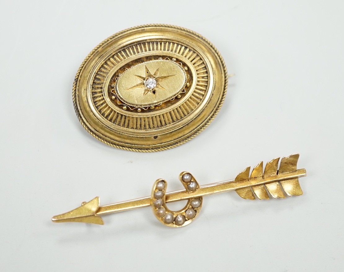 An early 20th century yellow metal, and seed pearl set arrow and horse shoe brooch, 60mm and a Victorian paste set yellow metal oval brooch.